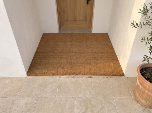 Paillasson coco naturel sur mesure ajusté à l'entrée, devant une porte en chêne